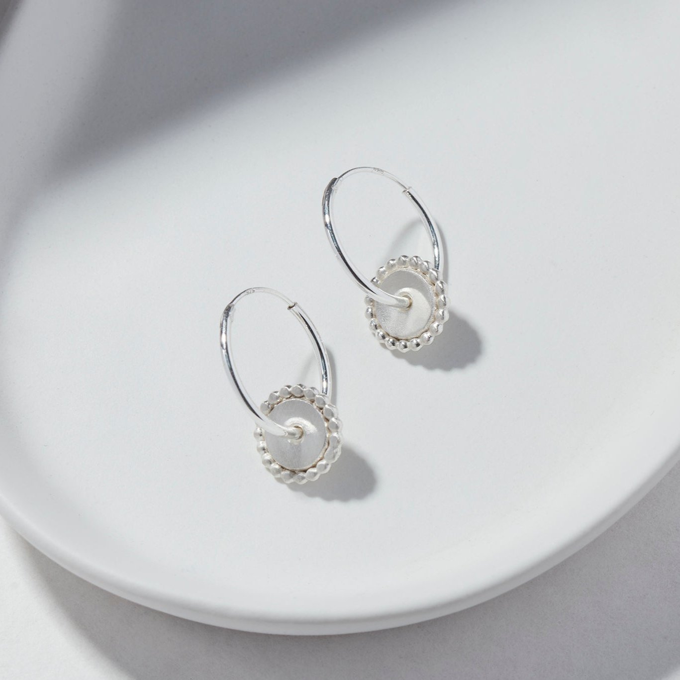 Sterling silver hoop earrings featuring a circular dotted disc, elegantly displayed on a white background.