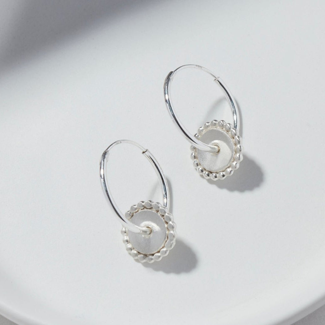 Sterling silver hoop earrings featuring a circular dotted disc, elegantly displayed on a white background.