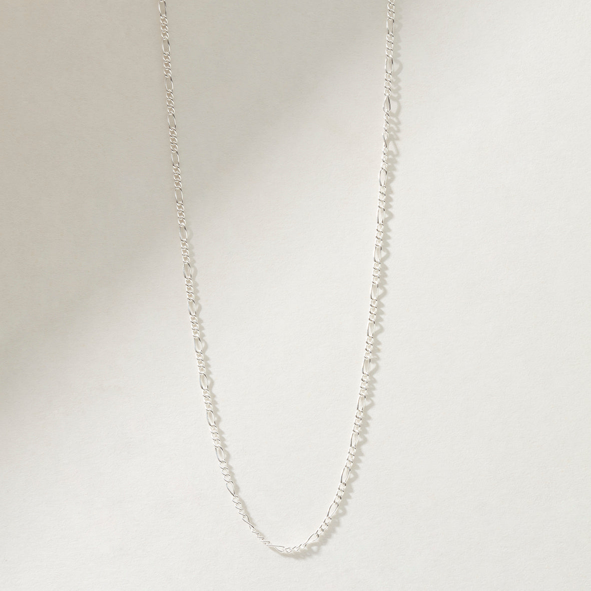 Close-up of sterling silver figaro chain necklace available in 16, 18, or 20-inch lengths, perfect for men and women, ideal for layering.

