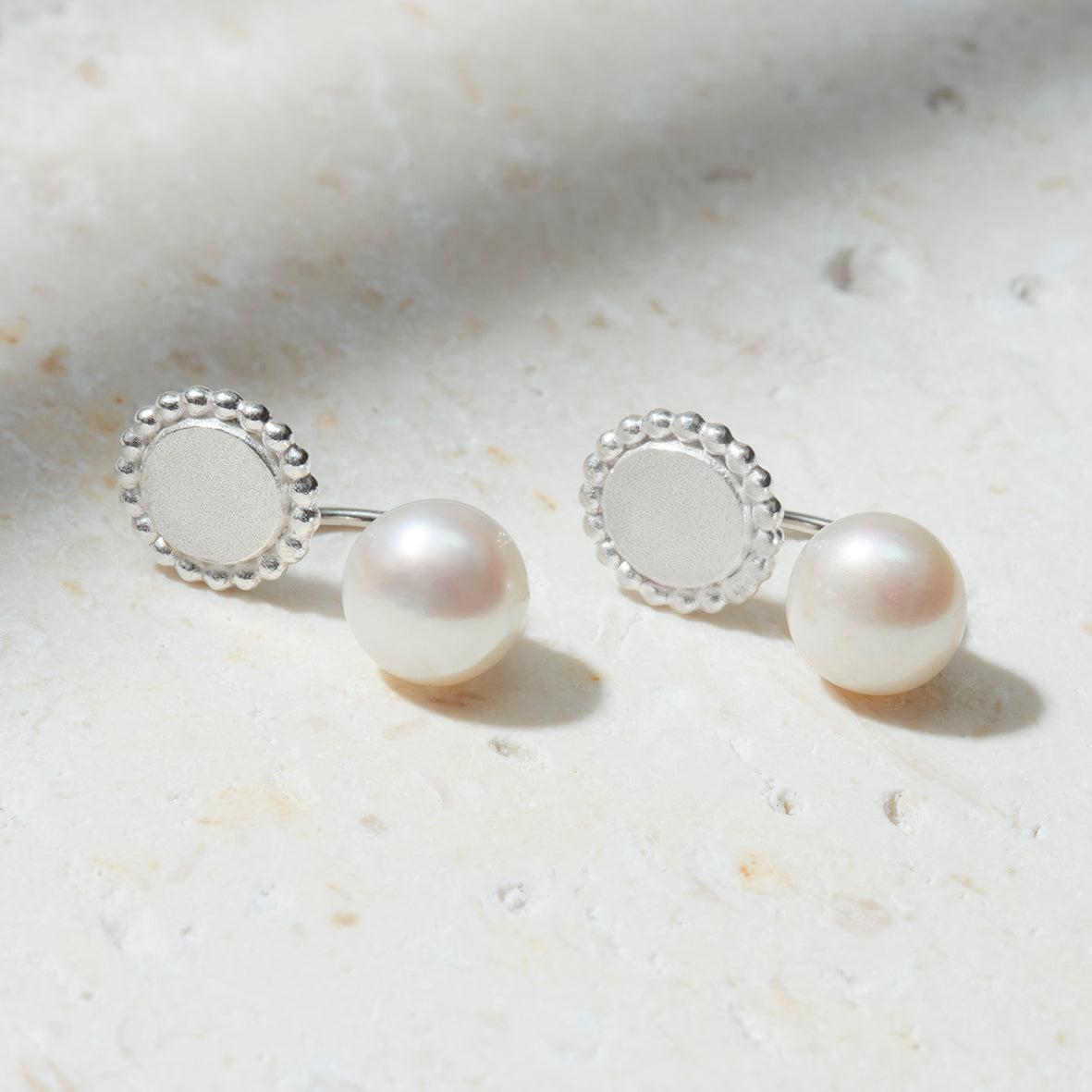 Sterling silver ear jackets with freshwater pearls and a detailed round silver disc with dotted edges.
