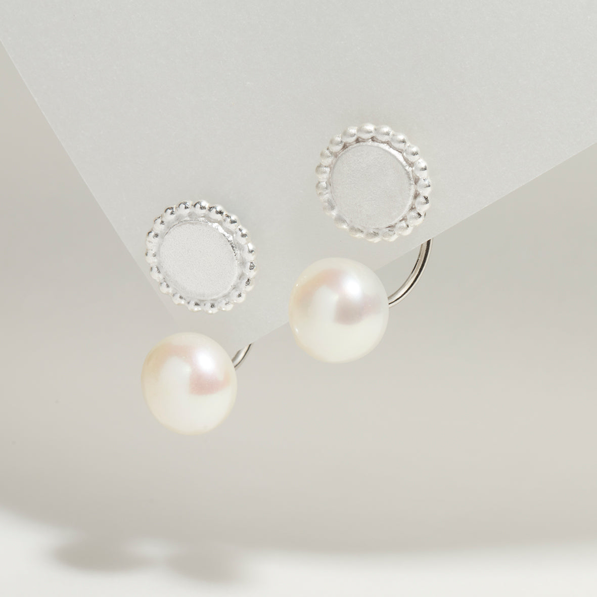 Sterling silver ear jackets with freshwater pearls and a detailed round silver disc with dotted edges.
