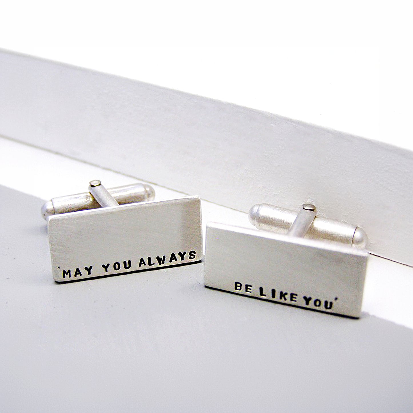 Close-up of personalised silver cufflinks, hand-stamped with custom text.