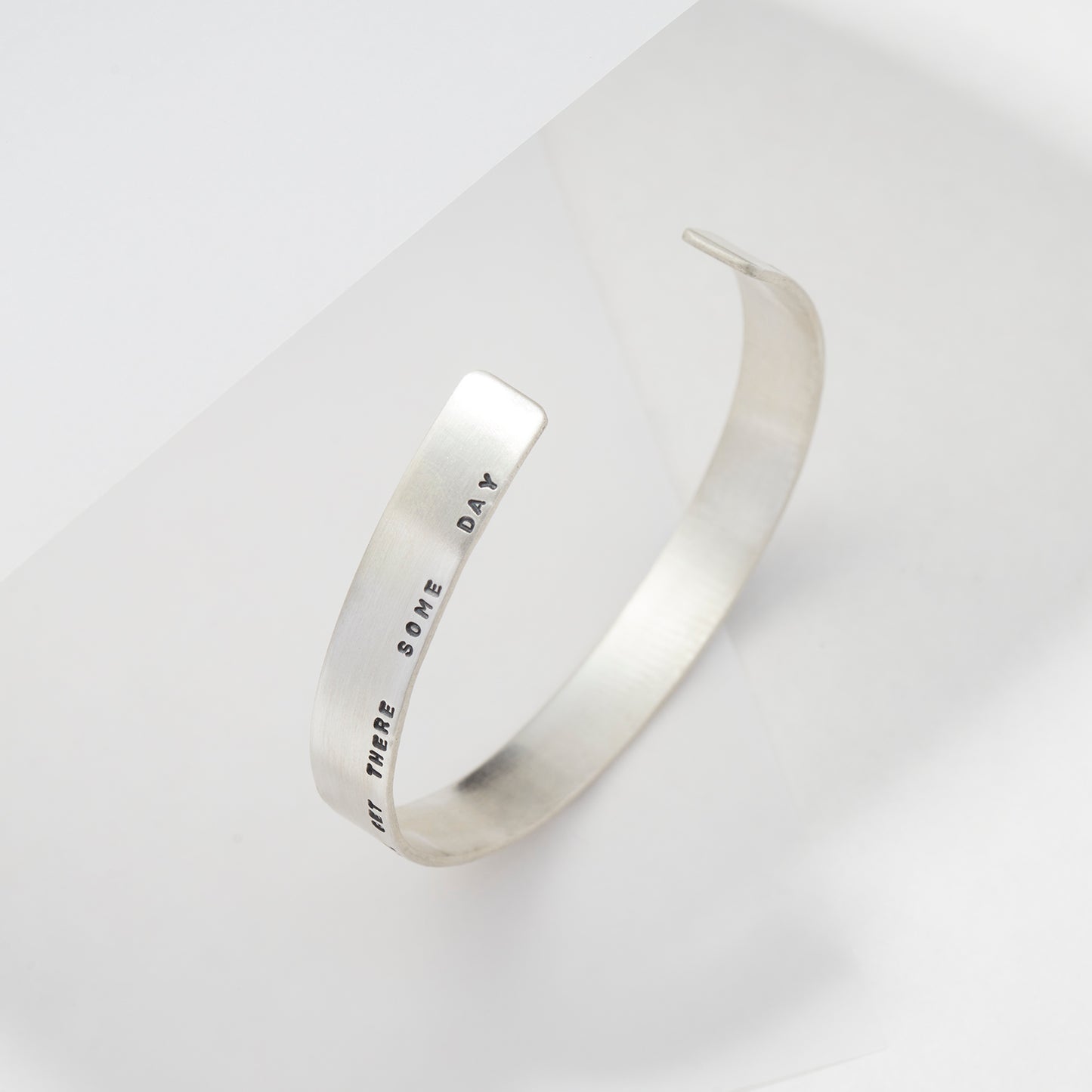 Handcrafted sterling silver cuff bracelet featuring a custom engraved message, displayed on a minimal white background.