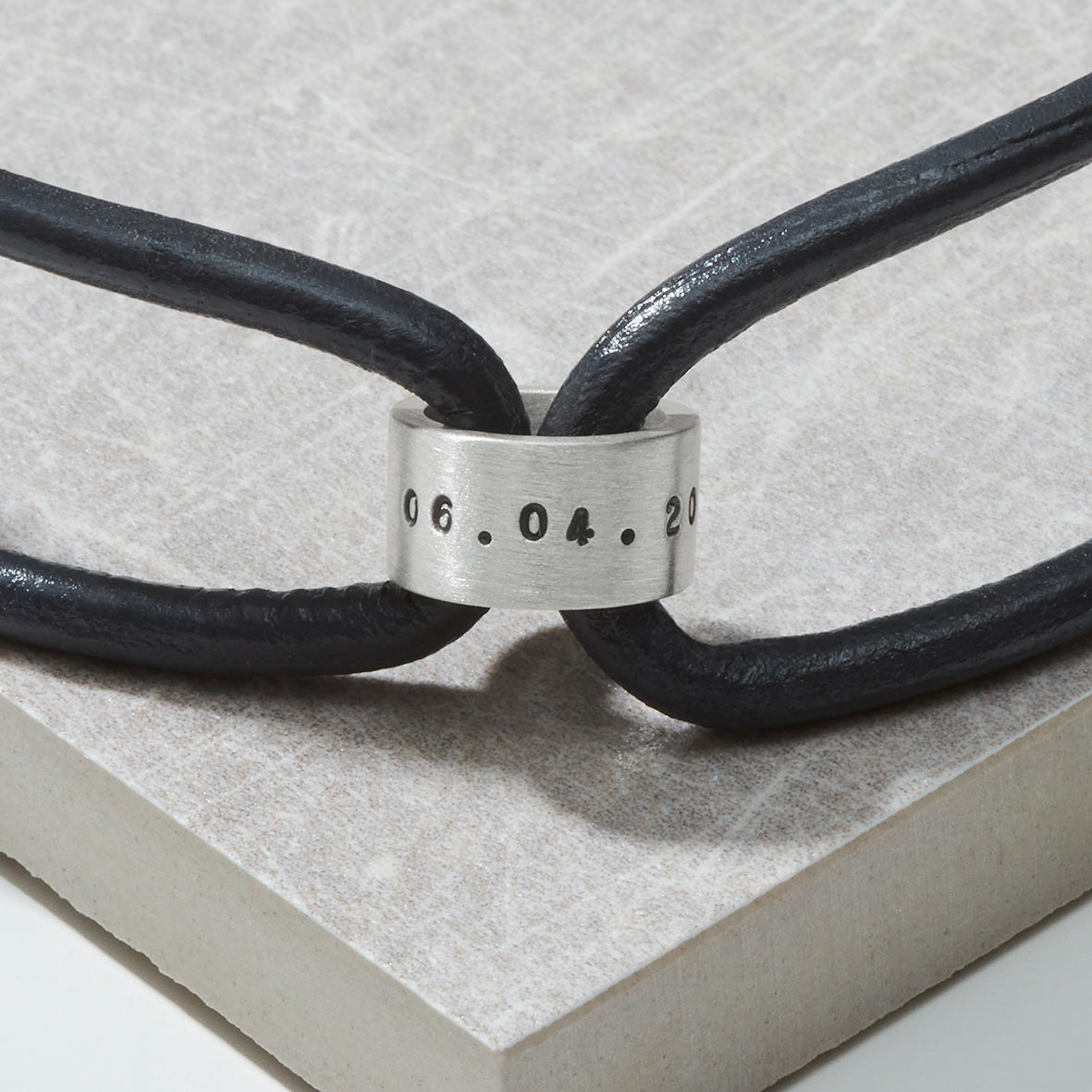 Close-up of the personalised silver story bead on a black leather cord, showing detailed hand-stamping