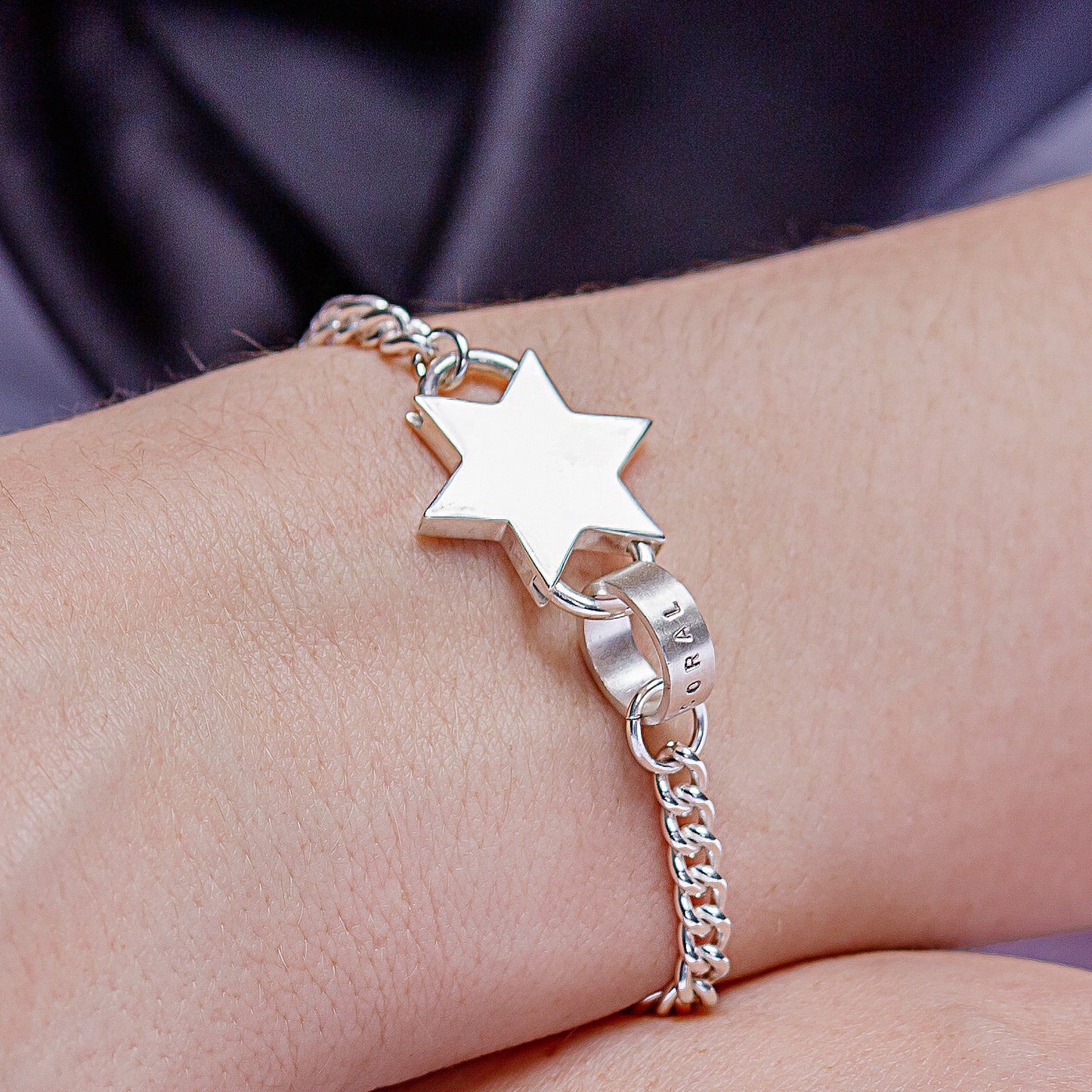 Close-up of a chunky silver star charm bracelet with a personalised hoop.
