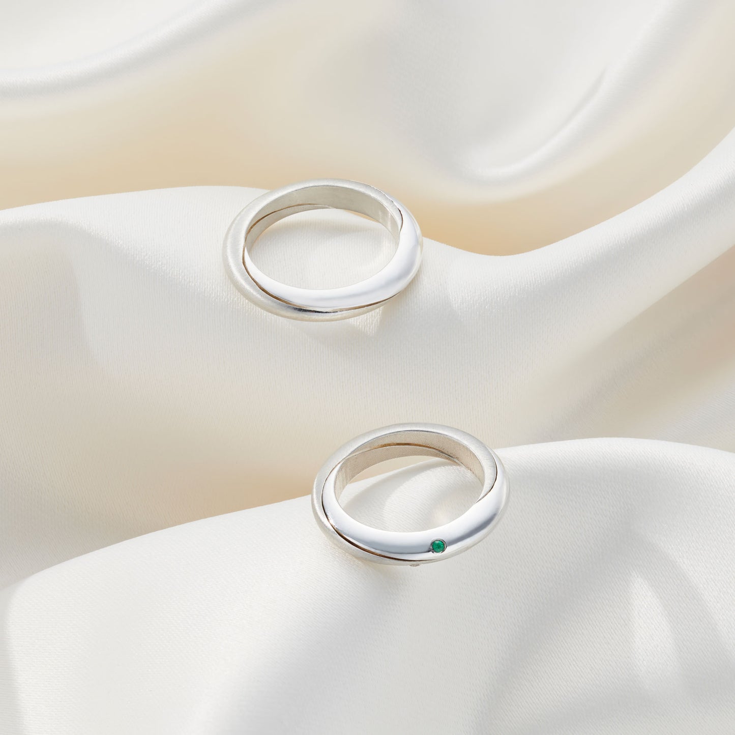 Gemstone accented Mobius rings with a polished finish, lying elegantly on fabric